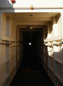 Interior corridor of large ship or vessel, looking down a long symmetrical passage with lighting and shadows. Metal structure of marine transport. Industrial architecture of ship.