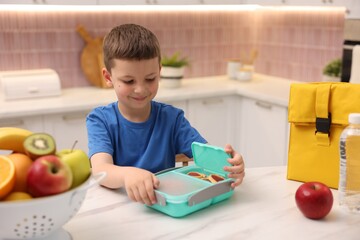 Boy packing lunch box at white marble table in kitchen
