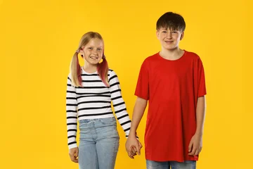 Brother and sister holding hands together on orange background © New Africa