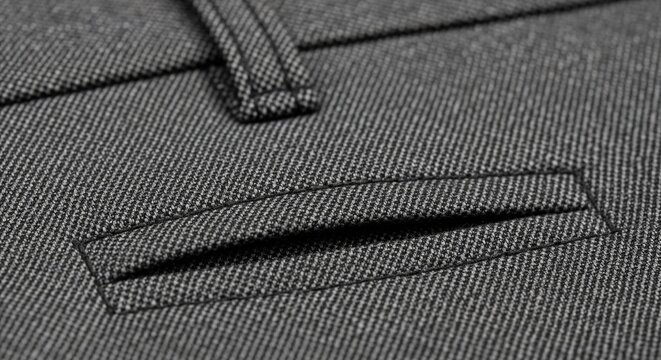 Macro photograph of a horizontal rear pocket on grey formal dress trousers showing clean stitching and fabric texture.