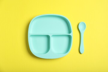Obraz premium Plastic section plate and spoon on yellow background, flat lay