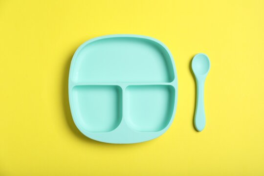 Plastic section plate and spoon on yellow background, flat lay