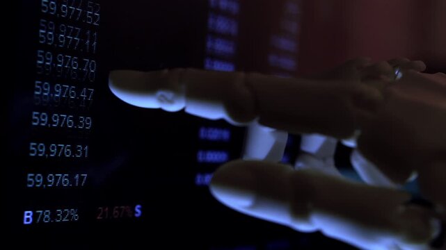 Humanoid robot hand monitoring economic graphs on a PC display. Macro low-key shot in a dark room representing AI business automation.