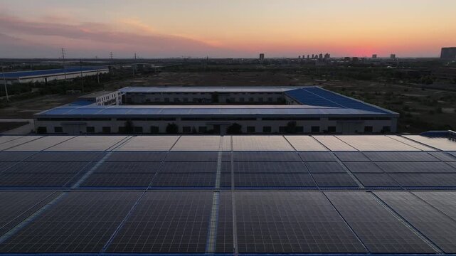 Solar panel array on industrial factory roof during sunset with distant city skyline
