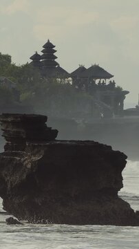 Misty Coastal Tanah Lot Temple Cliff At Sunrise, Solitary Pilgrim Imagined On Rocks, Waves Crashing Over Dark Basalt, Distant Hindu Shrine Silhouette, Tranquil Meditative Atmosphere, Vertical video