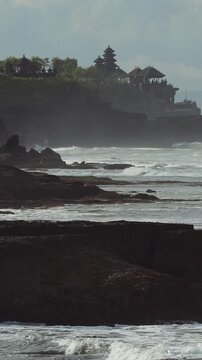 Soft Evening Tanah Lot Temple Silhouette On Cliff, Golden Haze And Calm Shallow Pools, Gentle Tide Lapping Basalt Shelf, Low Light Reflections And Meditative Travel Mood, Cultural Landmark Evoking