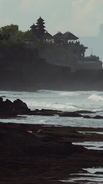 Wild Surf Crashing Against Tanah Lot Temple Cliff, Powerful Waves Smashing Volcanic Rocks With Thick Spray And Foam, Distant Pagoda Silhouette Framed By Stormy Sky,Bali island,Indonesia,vertical video