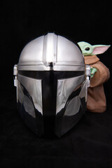 Obraz premium A shiny, metallic Mandalorian helmet on dark velvet, with Grogu holding onto the right side, captured in El Salvador, Cinepolis on June 26, 2026.