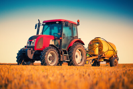 Red agricultural tractor with yellow tank trailer in wheat field at sunset