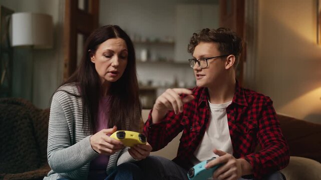Adolescent boy teaching his mom how to use a game controller, gaming at home