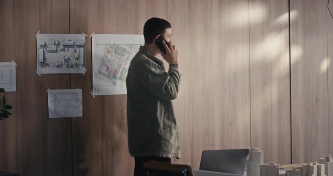 Man making a phone call in a planning office beside architectural models and maps
