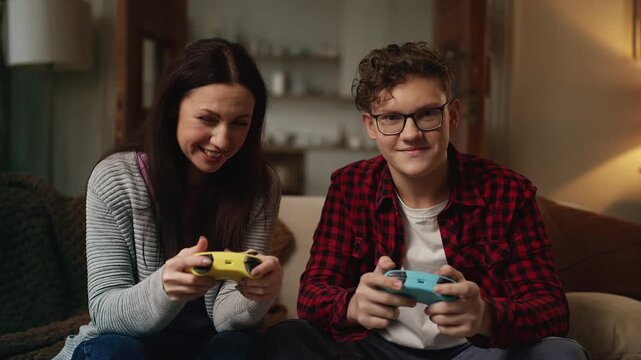 Portrait of cheerful teen son and his mom playing video games, family pastime