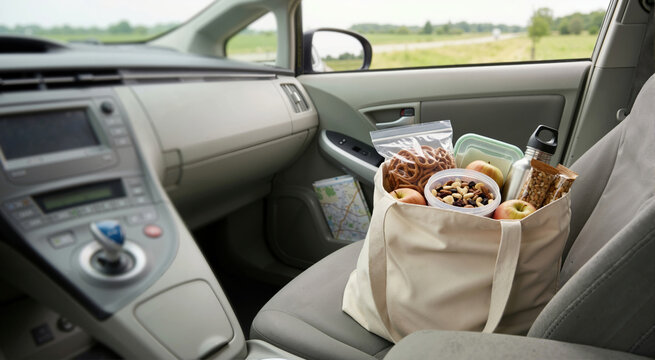 Canvas tote bag filled with healthy snacks and water bottle on a car passenger seat. Summer road trip preparation and travel concept