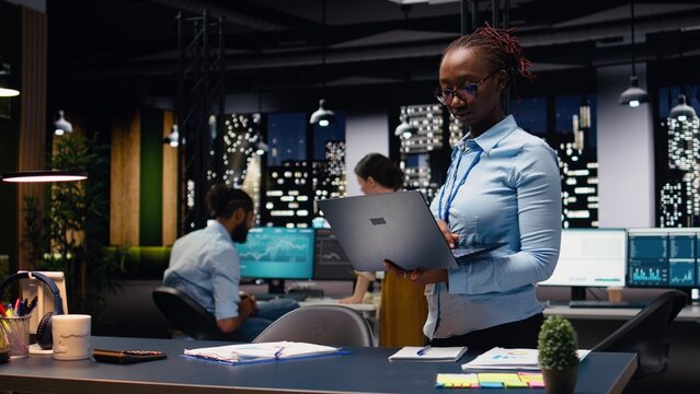 Portrait of african american woman in office managing schedules on laptop, organizing calendar appointments and meetings, Jolly young adult compiling company information records and data.