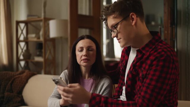 Teenage boy sharing his hobby with his mother, showing his online work on phone