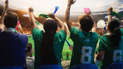 Fototapeta premium Rear view of football supporters holding drink cup while facing pitch, waving scarves for football fan and match day concepts.