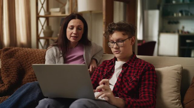Teenage boy explaining to his mother how to use an AI assistant on a laptop