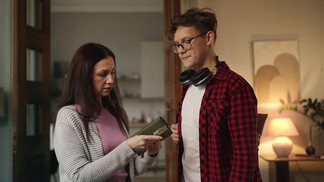 Mother giving money to her happy teen son wearing backpack, financial assistance