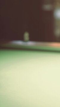 A collection of colorful pool balls sits neatly arranged on a green felt pool table. A cue stick rests beside them, ready for the next game. The setting has a casual atmosphere.