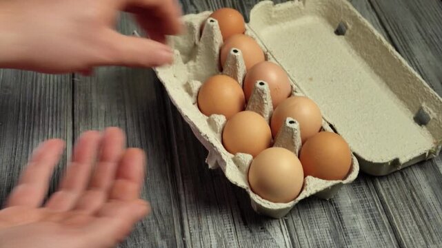 Hands of a person carefully selecting eggs from a carton, showcasing the process of transferring eggs to another hand in a well-lit kitchen setting