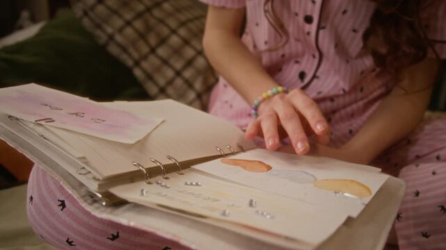 Caucasian teenager girl in pajamas flipping through handmade scrapbook with drawings and stickers. Clip is ideal for mental wellbeing, youth creativity, and hobby marketing campaigns