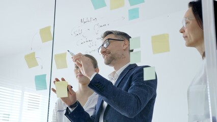 Business team brainstorming and collaborating in a modern office, mapping marketing strategy with colorful sticky notes on a glass board, planning projects and sharing ideas © volha_r
