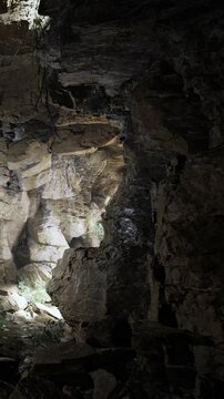 A group is inside a cave where light enters through an opening in the rocks. The dark walls show rough textures. People look around at the rocky formations.