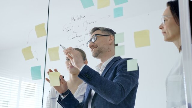 Business team brainstorming and collaborating in a modern office, mapping marketing strategy with colorful sticky notes on a glass board, planning projects and sharing ideas