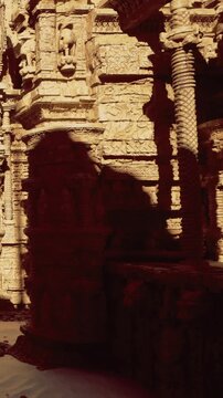 Light shines on detailed carvings of an ancient temple. Stone structures stand tall, showing signs of age. Sand surrounds the area creating a historical atmosphere.