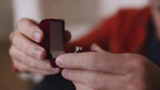 Close-up of male hands holding engagement ring in box, preparing to propose