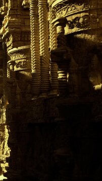 The walls display detailed carvings and designs in a historical site. Light from the setting sun casts shadows across the stone surfaces, creating patterns and textures.
