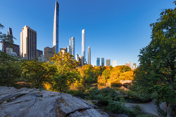 Fototapeta premium Central Park autumn foliage and rock formations with view of Billionaires' Row supertall skyscrapers. Midtown Manhattan, New York City