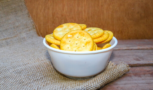 Round salty crackers served on a plate in a white bowl on a wooden table with jute sack. Crispy baked biscuit snack photographed from above. Top view Crispy baked biscuit snack with golden texture