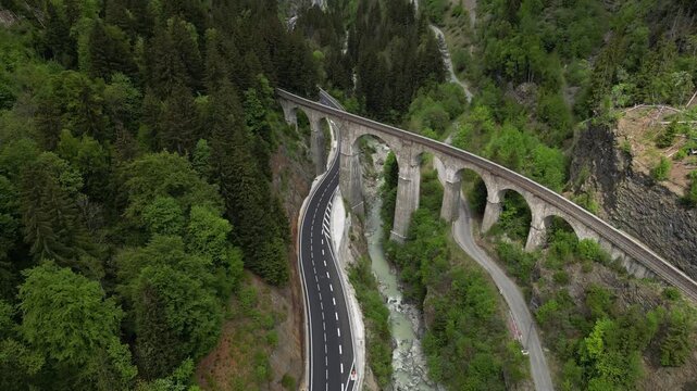 View of the historic stone railway viaduct crossing a dramatic alpine gorge with mountain road and snow-covered peaks near Chamonix in the French Alps