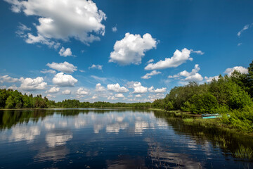 Fototapeta premium Scenic landscape of a calm lake in Karelia, Russia, with beautiful cumulus clouds reflecting in the mirror water