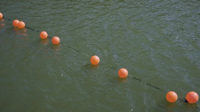 Orange floating buoys marking safety line across green harbor water