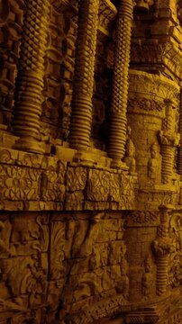 Detailed carvings cover the temple wall showing various figures and patterns. The sunlight highlights the artistry and structure. Visitors observe the craftsmanship at the historical site.