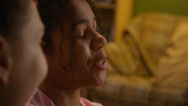 African American girl in striped pajamas holding photo of crush or love interest to chest while talking and smiling with friend during sleepover. Youth lifestyle, romance and friendship marketing