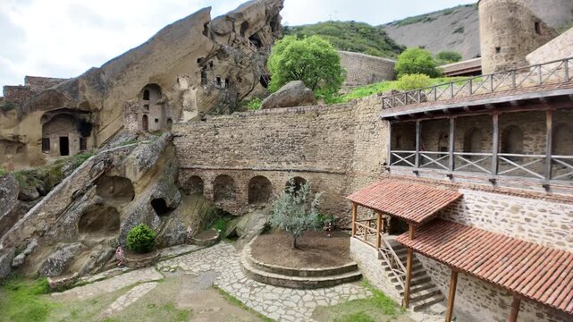 David Gareji monastery, a historic rock-hewn orthodox complex in Georgia, featuring multiple carved caves, ancient stone walls, and a green courtyard under a cloudy sky