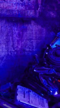 Metallic objects are scattered on the ground in a dim area. A blue light casts colorful reflections on the surface, creating a unique visual effect. The setting appears to be urban and industrial.