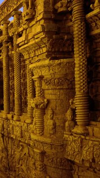 Visitors explore a carved stone wall featuring detailed sculptures and patterns. The setting is a historic site under soft evening light, showcasing artistry and craftsmanship.