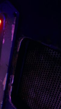 A speaker is displayed with glowing lights in a dark space. The speaker shows signs of wear on its surface. The lighting creates a moody atmosphere around the device.