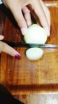 Close up of hands slicing peeled onion (bombay) with a knife on a wooden cutting board, fresh vegetable food preparation, cooking ingredient footage. 