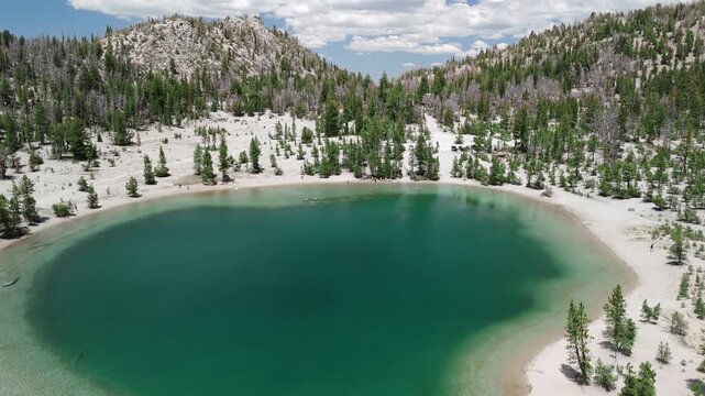 Sunny Summer Drone Flight Over Turquoise Mountain Lake with Snow and Pine Trees