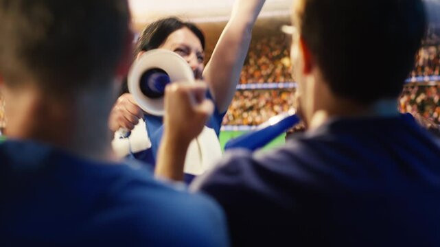 Energetic woman shouts through megaphone in stadium, leading football fans during match, showing female supporter galvanizing soccer crowd doing loud chants in sports arena for fan culture content.