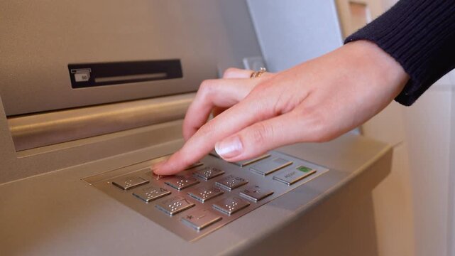 Close-up of a female hand entering a personal identification number on an automated teller machine keypad to perform a financial transaction and withdraw cash from her bank account