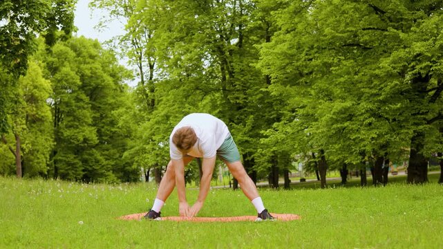 man performs a stretching workout on a yoga mat in a green park. This outdoor fitness exercise improves flexibility for a healthy, active lifestyle. High quality 4k footage