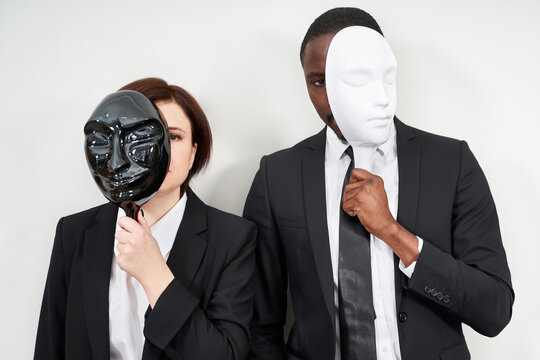 African man and Caucasian woman wearing black suits hiding face with plastic masks