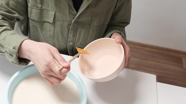 Close up of ceramic artist brushing thick glaze onto a bisque bowl. Process of glazing a ceramic bowl using a wide studio paintbrush 4k footage