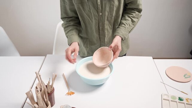 Artisan hands glazing a bisque ceramic bowl for an artistic finish. Applying thick decorative glaze to a pottery bowl with a wide brush 4k video